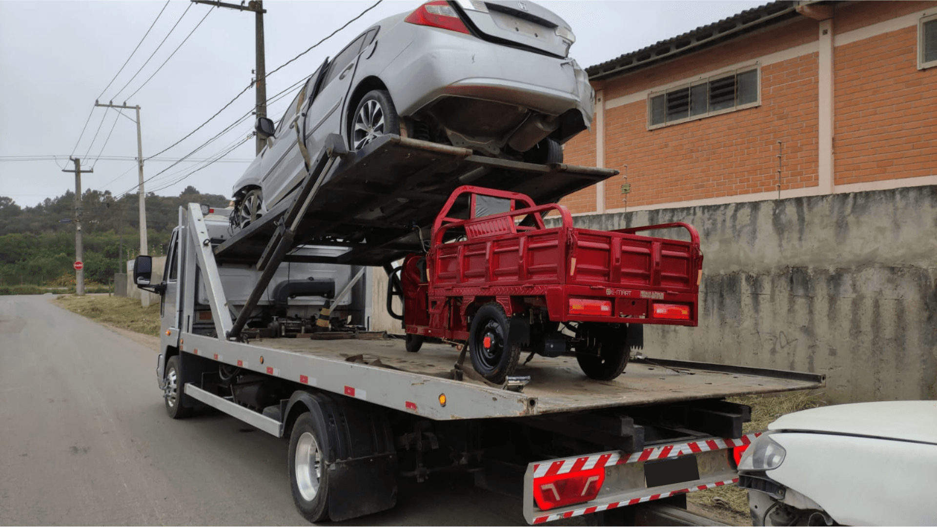 Uma foto mostrando a traseira do caminhão carregado com um carro em cima e um triciclo em baixo.