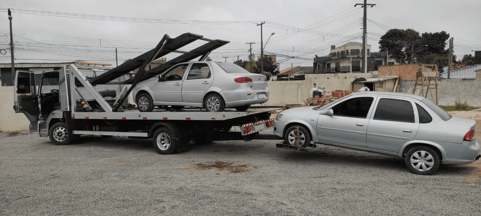 Uma foto mostrando a lateral do caminhão carregado com um carro em baixo e um carro sendo arrastado na traseira.